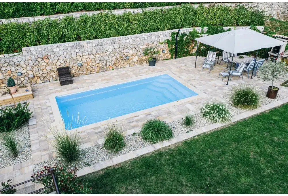 Blå rektangulär glasfiberpool Aruba med kaklad omgivning och grönskande bord