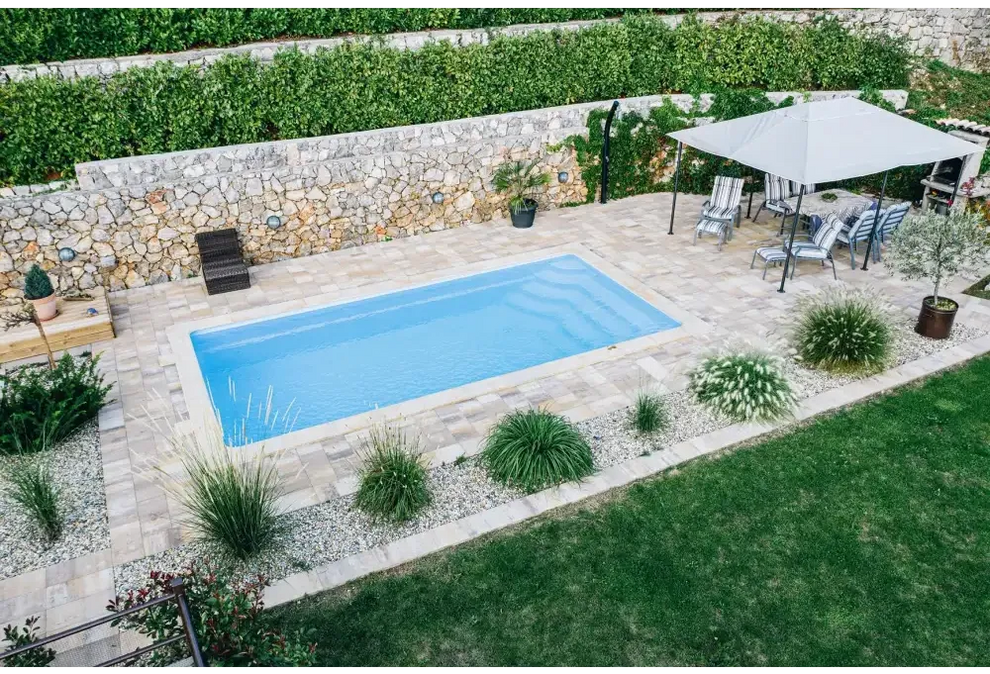 Blå rektangulär glasfiberpool Aruba med kaklad omgivning och grönskande bord