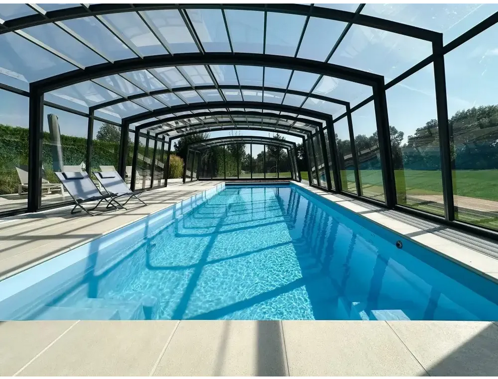 Lång rektangulär inomhuspool med klar blåvatten och svartramat glastak för Bahama trädgårdspool med transparent pooltak