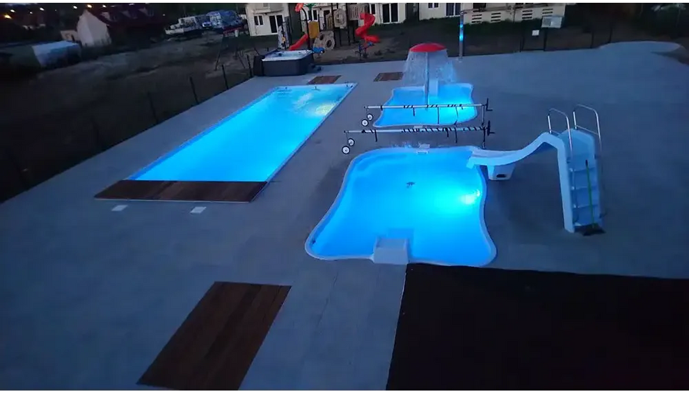 Blå upplyst Bahama trädgårdspool med rutschkanor, vattenfall och transparent pooltak