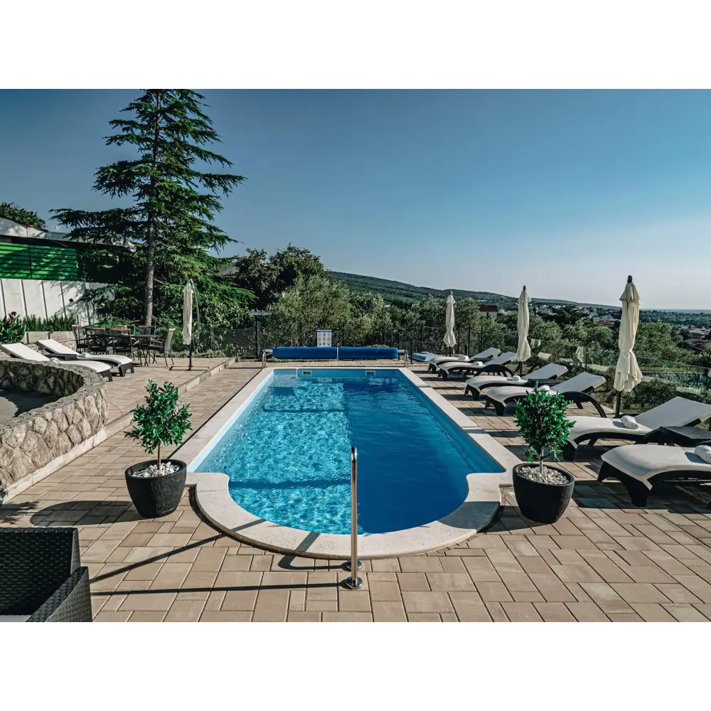 Glasfiberpool Barbados med klar blå poolvatten, stenplattor och krukväxter