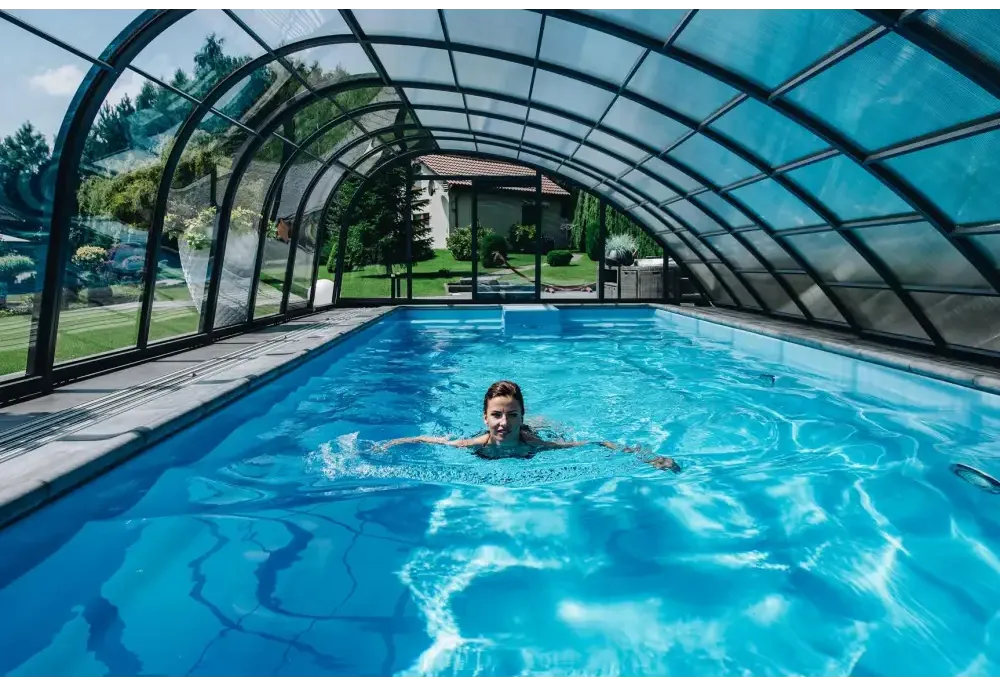Kvinna simmar i glasfiberpool Trinidad med blå kakel och inbyggt poolöverdrag under glastak